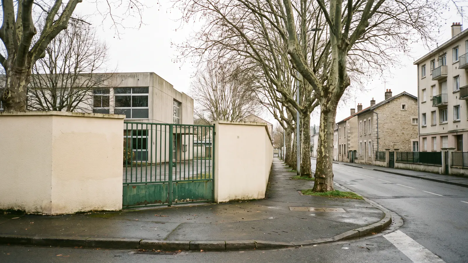 Entrée d'un collège public français vue depuis la rue, avec en arrière-plan un quartier résidentiel mêlant maisons individuelles et immeuble collectif.